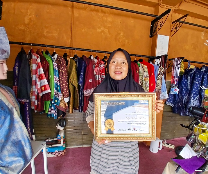 Wawa Ediny memegang piagam penghargaan dari BRI di kiosnya, kawasan Rumah Singgah Tuan Kadi, Pekanbaru, Riau. Foto: Surya/Riau1.